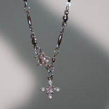 Cargar imagen en el visor de la galería, El collar Destello de estrella presenta dos colgantes en forma de estrella decorados con piedras claras, sobre un fondo gris claro suavemente iluminado.