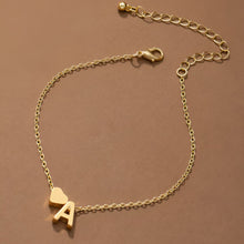 Cargar imagen en el visor de la galería, La Pulsera de tobillo con inicial, una delicada tobillera de oro con un pequeño dije de corazón y un dije de letra A, se muestra sobre un fondo marrón. Tiene una cadena ajustable con cierre de langosta y eslabones extensibles.