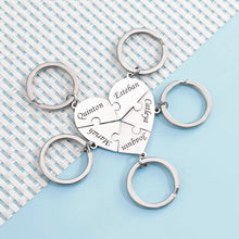 Cargar imagen en el visor de la galería, Cuatro piezas del Collar o llavero personalizado de piezas de rompecabezas, cada una grabada con un nombre distinto, forman un corazón sobre tejido azul y blanco-un regalo perfecto para seres queridos.