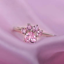 Cargar imagen en el visor de la galería, El Anillo Patita rosa es un delicado anillo de plata adornado con cinco gemas rosas en forma de pata, que se muestra sobre una suave tela rosa: perfecto como regalo para los amantes de las mascotas.