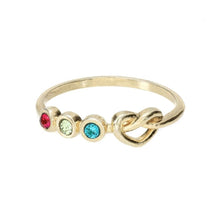 Cargar imagen en el visor de la galería, Anillo dorado personalizado Lazos del corazón con tres piedras redondas de nacimiento -roja, verde claro y azul- en hilera junto a un pequeño nudo en la banda, sobre un fondo blanco liso.