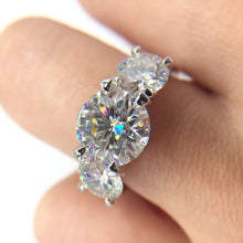 Cargar imagen en el visor de la galería, Primer plano de una mano que luce el Anillo Tres destellos de amor, con tres grandes circonitas redondas brillantes engastadas en acero inoxidable, siendo la piedra central la más grande.