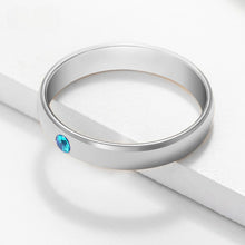 Cargar imagen en el visor de la galería, A simple Anillos apilables con nombres y piedras de nacimiento en color plateado, con una pequeña gema azul redonda incrustada en la banda, exhibidos sobre una superficie blanca bajo luz suave.