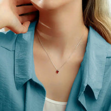 Cargar imagen en el visor de la galería, Una mujer con camisa celeste lleva un Collar con piedras de nacimiento personalizadas con un pequeño dije rojo, apoyando la mano en su cara-el regalo perfecto para mamá.