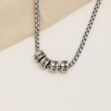 Cargar imagen en el visor de la galería, A Collar de cadena con dijes personalizados en plata, con cuatro dijes grabados con los nombres Roman, Emilie, Alexa y David, expuestos sobre una superficie beige clara.