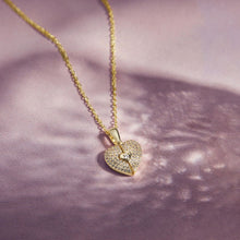 Cargar imagen en el visor de la galería, El Collar de Corazón Cofre personalizado presenta un colgante en forma de corazón con piedras brillantes y un motivo de ojo de cerradura, elegantemente engastado sobre un fondo de suave textura rosa claro.