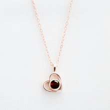 Cargar imagen en el visor de la galería, El Collar de corazón con foto es una delicada cadena en oro rosa con colgante en forma de corazón y gema roja, ideal para guardar recuerdos especiales, bellamente presentado sobre fondo blanco.