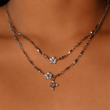 Cargar imagen en el visor de la galería, Primer plano del cuello de una persona que lleva dos collares de plata en capas, uno de los cuales es el Collar Destello de estrella. Ambos llevan delicados colgantes en forma de estrella adornados con piedras brillantes.