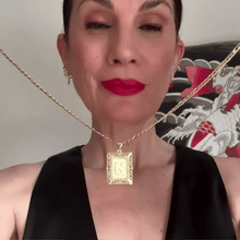 Cargar imagen en el visor de la galería, Una mujer con los labios pintados de rojo y un top negro sin mangas luce el collar colgante Collar IZAC con inicial personalizada. En el fondo aparecen ilustraciones decorativas en rojo, blanco y gris.