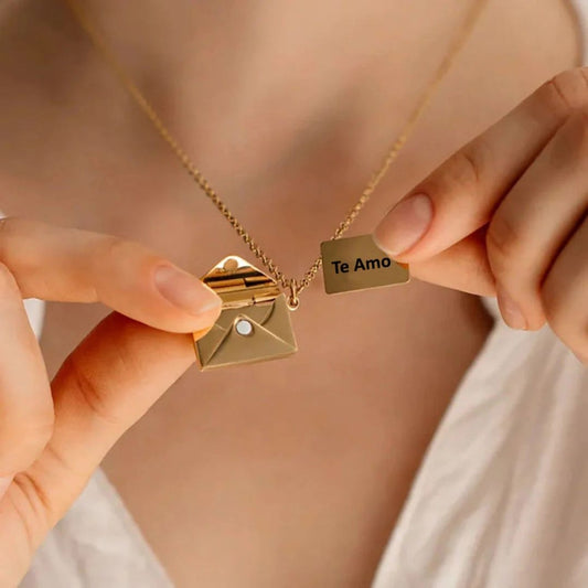Una persona viste un top blanco y sostiene el collar "Mi carta de amor", un collar de oro con un colgante en forma de sobre que se abre para revelar una pequeña nota de oro grabada con la inscripción "Te Amo", un regalo ideal para su esposa.