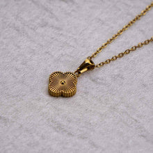Cargar imagen en el visor de la galería, El collar Trébol con inicial - ¡Lévate 2 por el precio de 1! es una cadena de acero inoxidable dorado con un colgante de trébol de cuatro hojas texturizado, que se muestra sobre un fondo de tela gris claro texturizado.