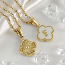 Cargar imagen en el visor de la galería, Dos colgantes Collar Trébol con inicial descansan sobre satén blanco. Uno presenta una letra E dorada con cristales transparentes; el otro muestra un motivo de rayos de sol con textura. ¡Lévate 2 por el precio de 1!.
