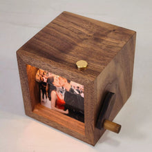 Cargar imagen en el visor de la galería, El Marco fotográfico con manivela muestra la imagen de una pareja besándose en una escena al aire libre, visible en ventana rectangular, con perilla de latón arriba y manivela lateral; un regalo conmemorativo memorable.