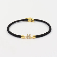 Cargar imagen en el visor de la galería, Pulsera ajustable con inicial (2X1): pulsera negra trenzada con extremos dorados y charm K en oro brillante. ¡Personaliza tu estilo y aprovecha la súper oferta 2x1!.
