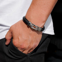 Cargar imagen en el visor de la galería, Una persona con camisa blanca y pantalones oscuros tiene la mano en el bolsillo, mostrando la Pulsera con nudo infinito - A mi hijo con un broche plateado en forma de nudo en la muñeca.