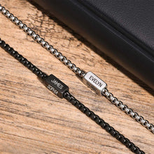 Cargar imagen en el visor de la galería, A pulsera de cubo personalizada en plateado, con los nombres "EVELYN" y "THOMAS" grabados, descansa junto a un artículo de cuero negro. Es el regalo perfecto para papá en el Día del Padre.