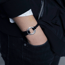 Cargar imagen en el visor de la galería, Una persona con jeans y chaqueta negros, camiseta blanca con pequeños estampados, lleva su mano en el bolsillo mostrando una Pulsera de cuerda para hombre grabada; un regalo ideal para él.