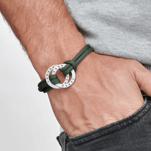 Cargar imagen en el visor de la galería, Una persona lleva la Pulsera de cuerda para hombre grabada con un colgante redondo plateado, combinándola con unos vaqueros oscuros y una camisa gris claro: un regalo personalizado para hombre ideal.