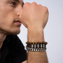 Cargar imagen en el visor de la galería, Un hombre lleva tres pulseras-una de cuentas marrones, otra de cuero trenzado con detalles metálicos, y la Pulsera de cuero para Papá personalizada con nombres-mientras reposa su barbilla en la mano. Ideal como regalo para hombre.