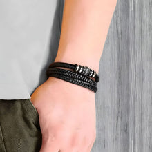 Cargar imagen en el visor de la galería, Un hombre con camisa blanca y pantalón verde lleva la pulsera de cuero "Siempre contigo Papá" con detalles plateados en la muñeca, ideal para regalar a padres, sobre fondo de madera gris.