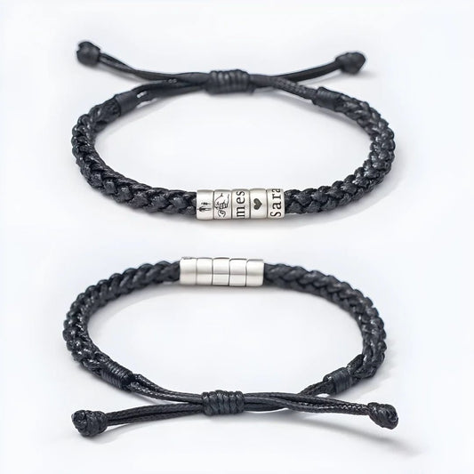 Dos pulseras negras "El mejor Papá" con nudos ajustables sobre fondo blanco: una lleva cuatro cuentas plateadas grabadas con caras de dibujos animados y "Tiempos tristes", mientras que la otra lleva cuentas plateadas lisas. Ambas son totalmente personalizables.