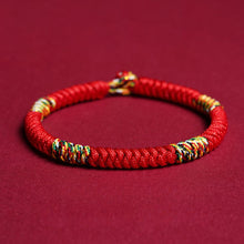 Cargar imagen en el visor de la galería, La Pulsera Hilo rojo del destino (Oferta 2X1) es una pulsera trenzada con hilos multicolores sobre fondo rojo, ideal como amuleto de la suerte y protección energética.