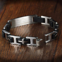 Cargar imagen en el visor de la galería, La Pulsera personalizada con frase para hombre, fabricada en acero inoxidable con segmentos metálicos y negros entrelazados, presenta un acabado cepillado y un diseño geométrico, elegantemente desplegado sobre una superficie de madera.