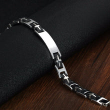 Cargar imagen en el visor de la galería, La Pulsera personalizada con frase para hombre, de acero inoxidable en tono plateado y negro con eslabones geométricos, se exhibe sobre una superficie negra texturizada y fondo de madera-un regalo ideal para hombre.