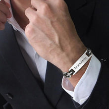 Cargar imagen en el visor de la galería, Un hombre con traje oscuro se ajusta el cuello de la camisa y lleva una Pulsera personalizada con frase para hombre grabada con "Te amamos", el regalo perfecto para hombre.