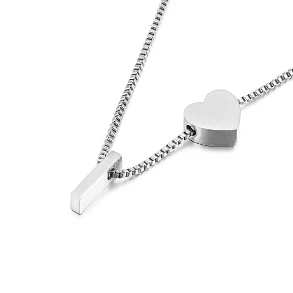 Un collar de cadena de plata con una barra rectangular y un colgante de corazón sobre fondo blanco, perfecto para combinar con la Pulsera de tobillo con inicial en color plateado y conseguir un elegante conjunto a juego.