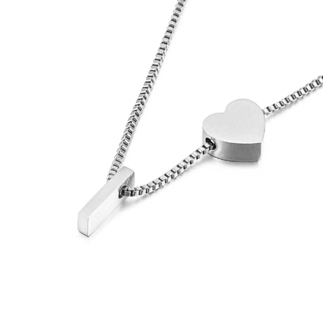 Un collar de cadena de plata con una barra rectangular y un colgante de corazón sobre fondo blanco, perfecto para combinar con la Pulsera de tobillo con inicial en color plateado y conseguir un elegante conjunto a juego.