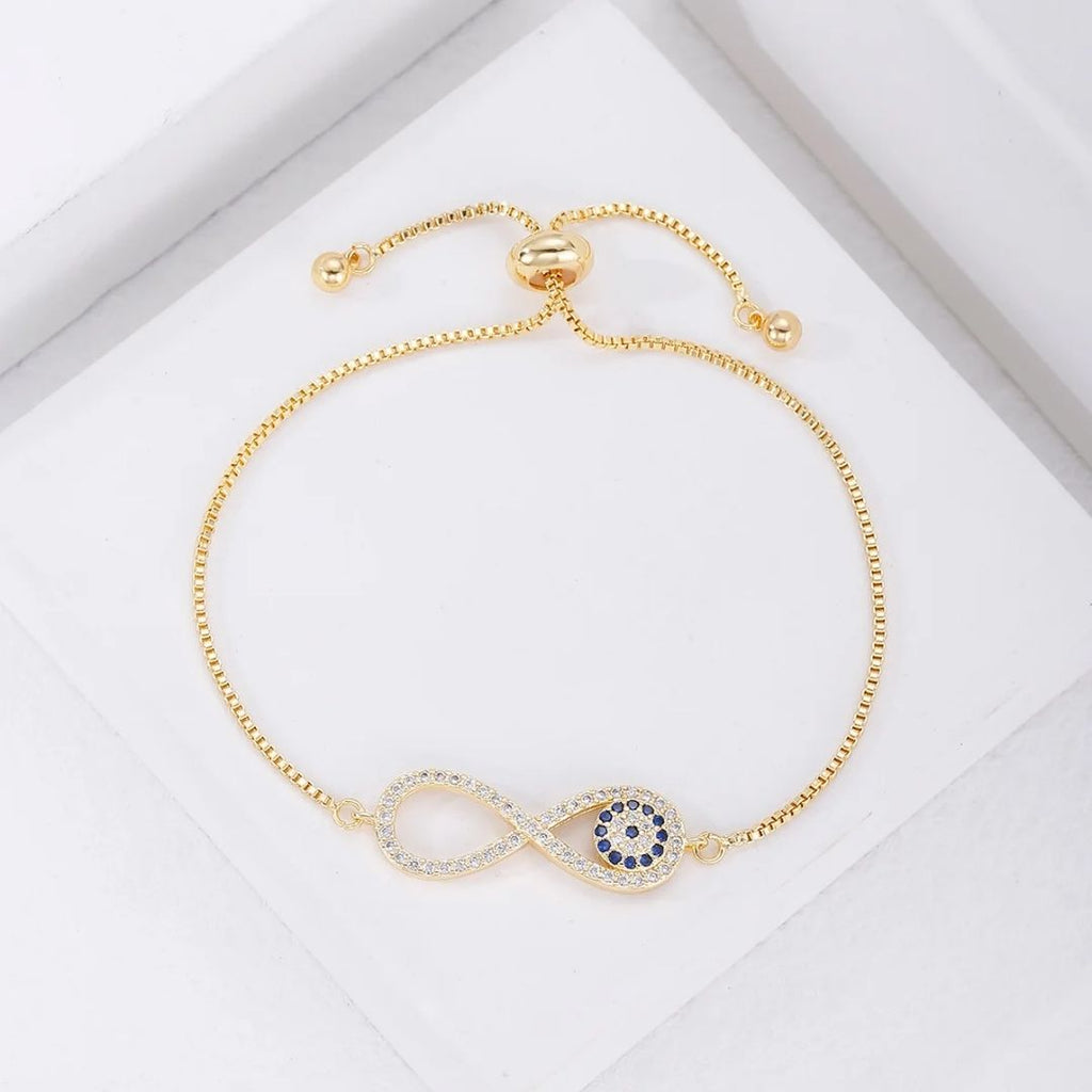 La Pulsera Infinito con ojo turco (OFERTA 2X1) es una pulsera ajustable de oro con un símbolo de infinito y piedras azules, inspirada en la tradicional pulsera de ojo turco para la protección contra la energía negativa, que se muestra sobre un fondo blanco.