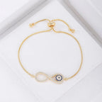 La Pulsera Infinito con ojo turco (OFERTA 2X1) es una pulsera ajustable de oro con un símbolo de infinito y piedras azules, inspirada en la tradicional pulsera de ojo turco para la protección contra la energía negativa, que se muestra sobre un fondo blanco.