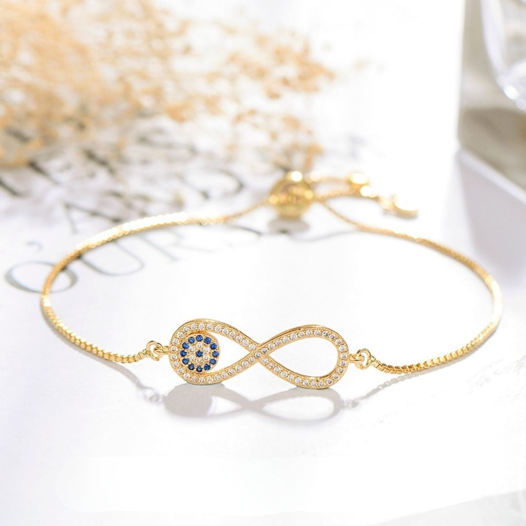 La Pulsera Infinito con ojo turco (OFERTA 2X1) es una delicada pulsera de oro con un símbolo de infinito adornado con piedras blancas y gemas azules, inspirada en la tradicional pulsera de ojo turco para la protección contra la energía negativa.