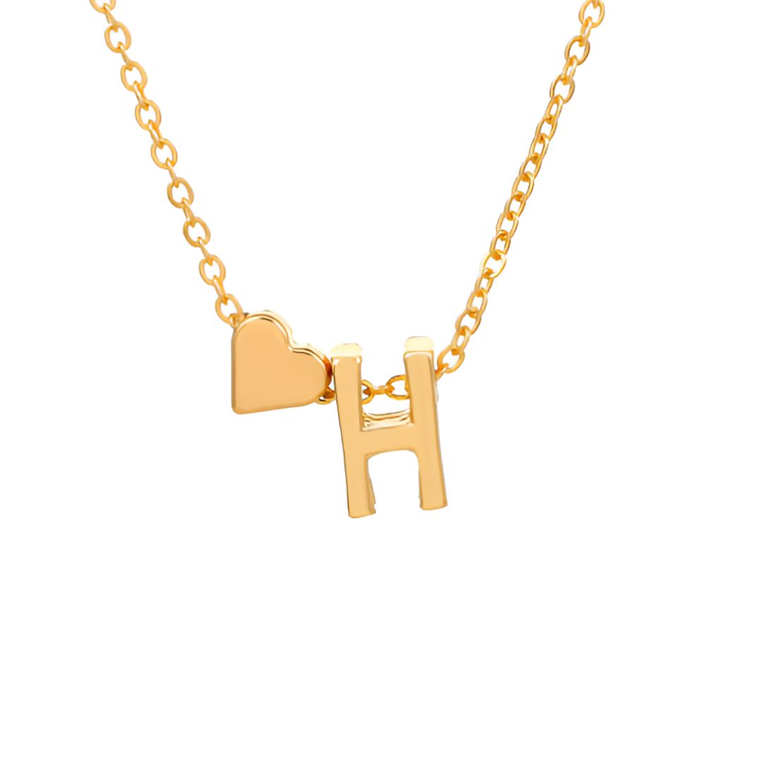 Un collar de oro con una delicada cadena exhibe un pequeño dije de corazón y un atrevido colgante en forma de H, ambos en oro, sobre un fondo blanco-perfecto para combinar con la Pulsera de tobillo con inicial en color dorado.