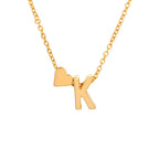 Un collar dorado con un pequeño corazón y la letra K como colgante cuelga de una delicada cadena dorada - combínalo con la Pulsera de tobillo con inicial dorado para un look coordinado.