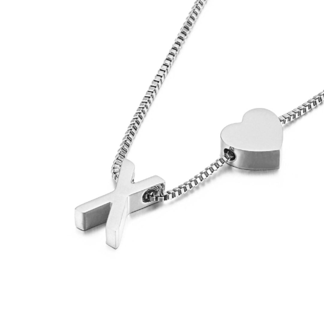 Un primer plano de un collar plateado con un dije de cruz y corazón en una cadena de caja junto a la Pulsera de tobillo con inicial, ambos en elegantes tonos plateados sobre un fondo blanco liso.