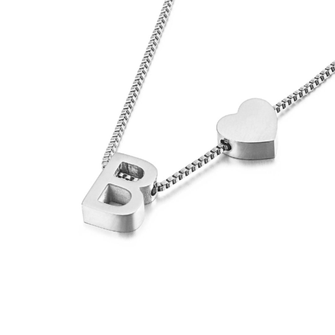 La Pulsera de tobillo con inicial en plateado presenta un dije de letra B en bloque y un pequeño dije de corazón en una delicada cadena, desplegados sobre un fondo blanco.