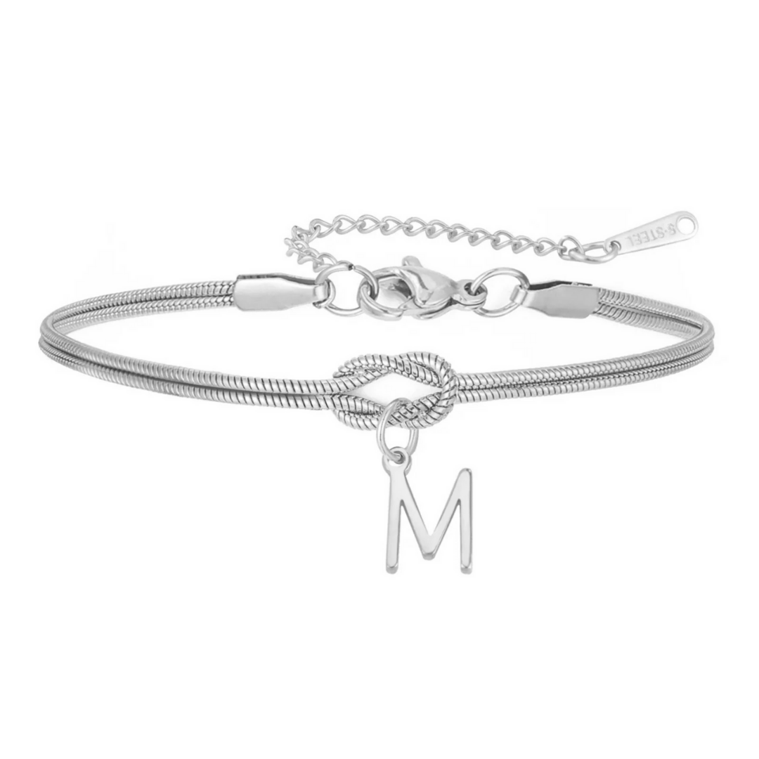 La Pulsera de nudo con inicial es de plata, con diseño de cadena serpiente, nudo central y charm colgante con letra M. Tiene cierre de langosta y cadena ajustable, perfecta como pulsera personalizada y un regalo inolvidable.