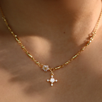 Primer plano del collar Destello de estrella en dorado, con un pequeño colgante en forma de flor con gemas diminutas y un colgante más grande en forma de diamante adornado con piedras brillantes, que se lleva alrededor del cuello.