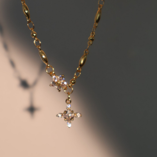 El Collar Destello de estrella es un collar bañado en oro con dos dijes de estrella decorados con cristales, destacando sobre un fondo degradado.