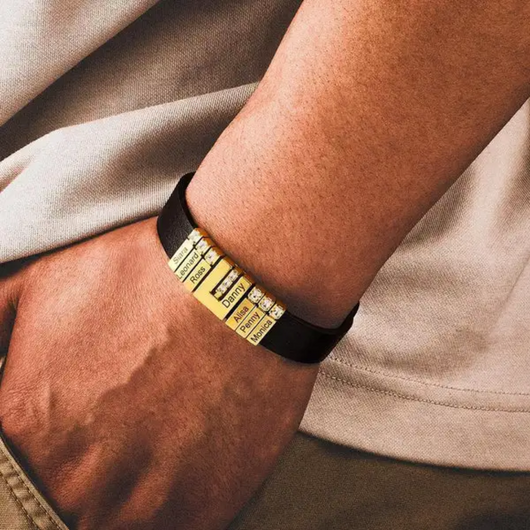 Una persona lleva en la muñeca la Pulsera de cuero personalizada con nombres, hecha de cuero negro y cuentas doradas grabadas, ideal como regalo único para papá. Combinada con una camisa beige clara, refleja elegancia y significado.
