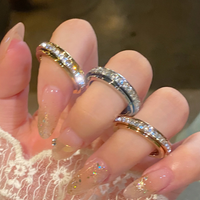 Una mano con largas y brillantes uñas desnudas sostiene tres anillos brillantes, entre ellos el Anillo giratorio Serenidad, perfecto para aliviar el estrés y la ansiedad. La persona lleva un delicado guante de encaje.