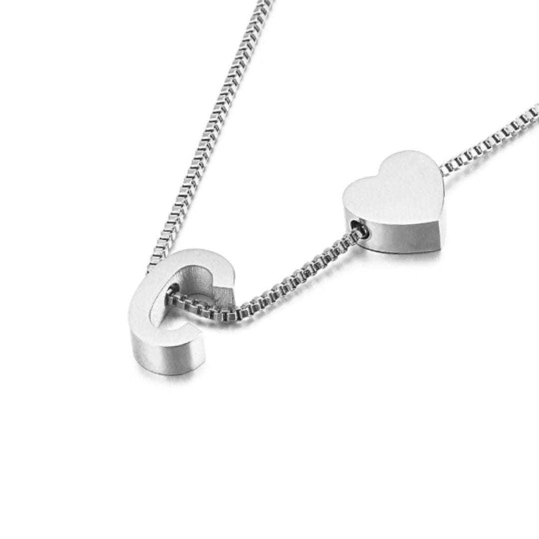 Un collar de plata con cadena de caja y dos colgantes -un corazón y la letra C- combina a la perfección con la Pulsera de tobillo con inicial en plateado para un look coordinado.