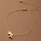 La Pulsera de tobillo con inicial, una delicada tobillera de oro con un pequeño dije de corazón y un dije de letra A, se muestra sobre un fondo marrón. Tiene una cadena ajustable con cierre de langosta y eslabones extensibles.