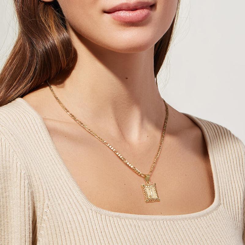 Una mujer lleva un top beige acanalado y el Collar Marco con inicial personalizada (Oferta 2x1), un colgante de oro con un dije rectangular ornamentado. La imagen está recortada para mostrar el cuello, el pecho y parte de la cara.