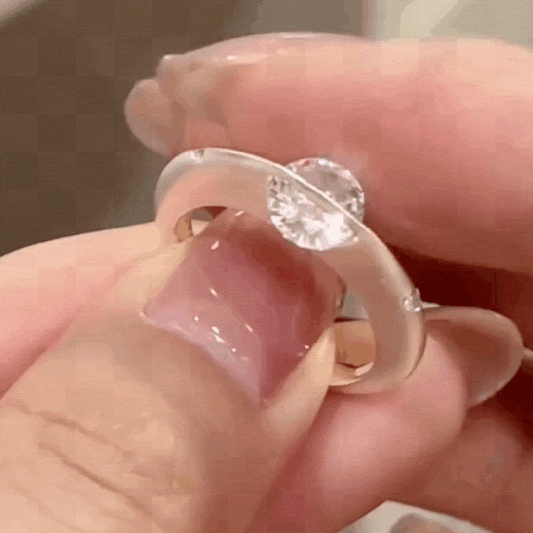 Primer plano de una mano sosteniendo el Anillo giratorio estelar, con un gran diamante redondo engastado en el centro que resalta su brillante gema y su banda pulida y ajustable.