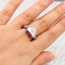 Cargar imagen en el visor de la galería, Primer plano de una mano que lleva el Anillo Abrazo al cielo personalizado con la cara en forma de corazón grabada &quot;best mom ever&quot;. La banda plateada tiene detalles decorativos, perfectos como anillo urna conmemorativo, sobre una superficie de madera blanca.