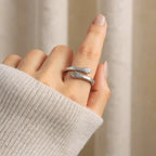 Una mano lleva el Anillo Abrazo - "Mi preciosa hija", un anillo de plata ajustable con forma de tenedor, con púas y mango visibles, sobre un suave fondo beige. La persona lleva un jersey ligero de canalé, un regalo ideal para hija.