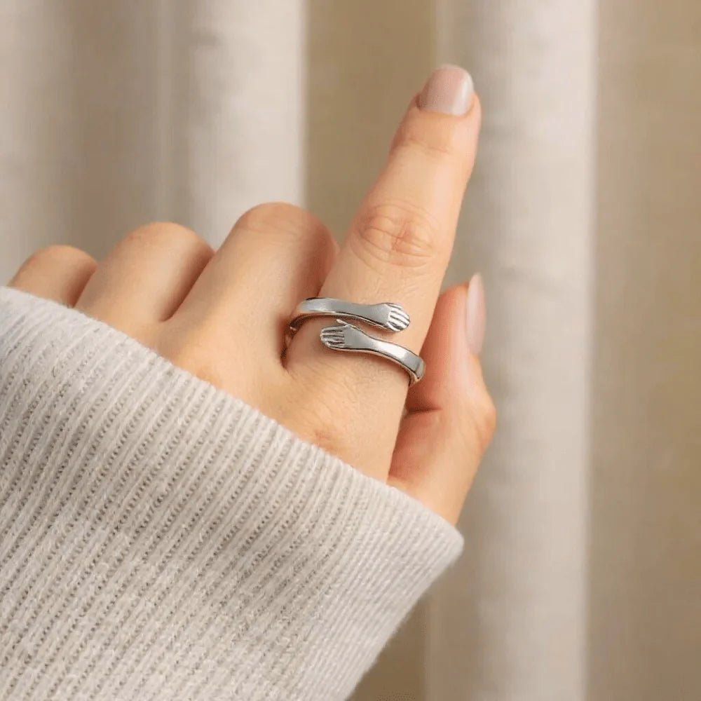 Una mano lleva el Anillo Abrazo - "Mi preciosa hija", un anillo de plata ajustable con forma de tenedor, con púas y mango visibles, sobre un suave fondo beige. La persona lleva un jersey ligero de canalé, un regalo ideal para hija.